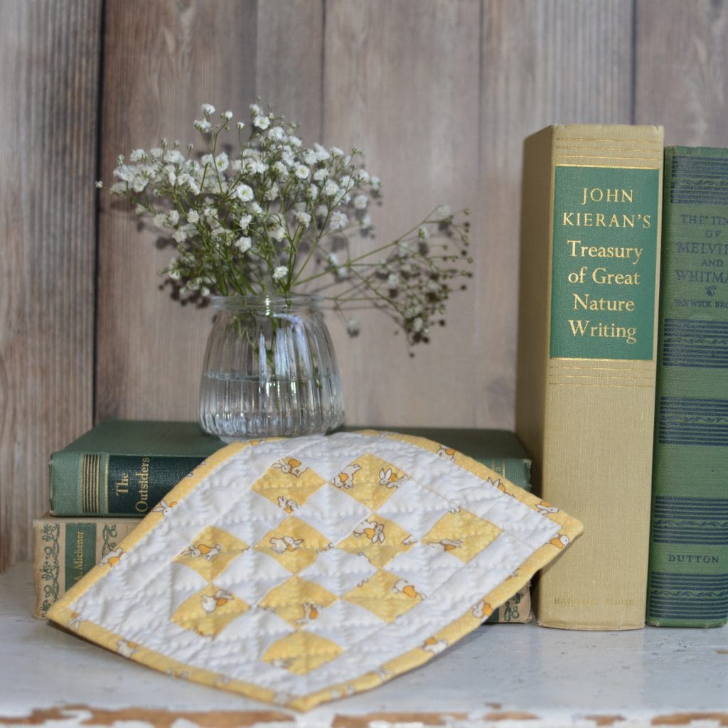 Little quilt on books with vase of flowers
