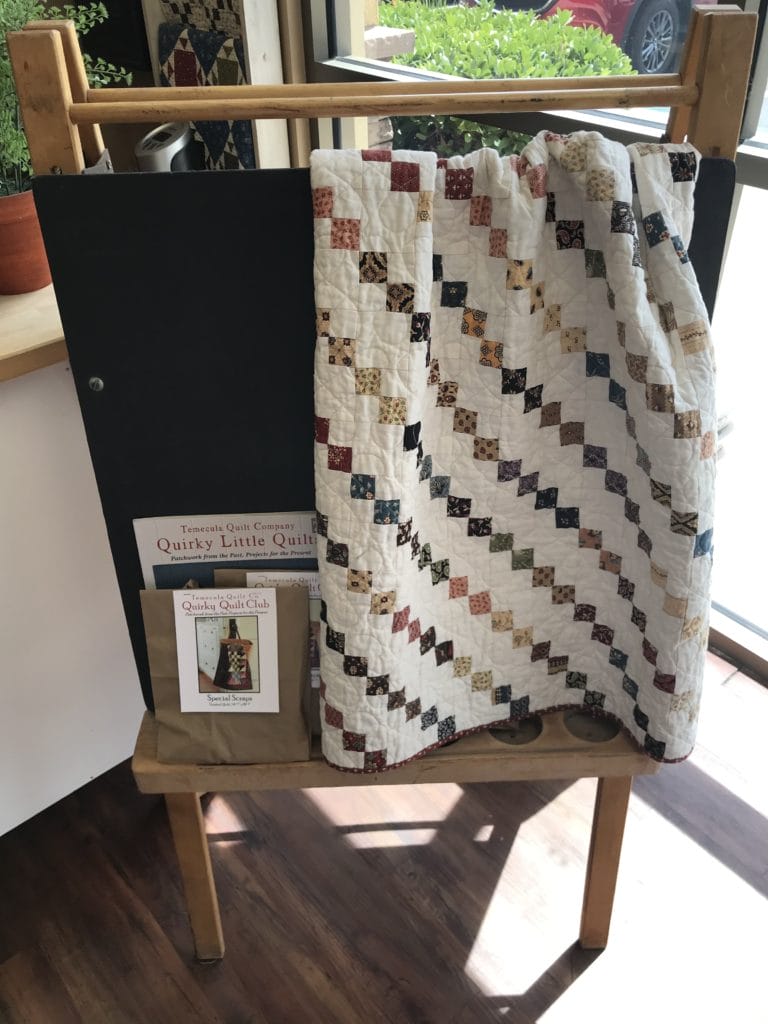 Four-patch quilt on easel with kit and Quirky Quilts book.
