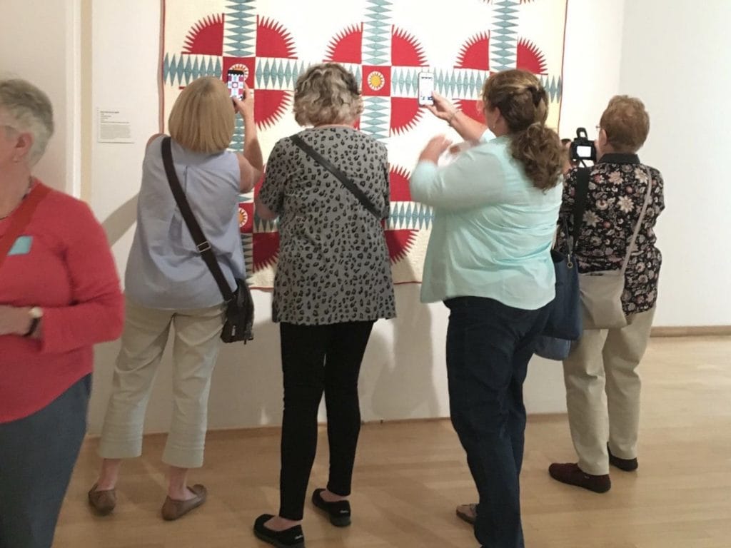 Women in museum taking picture of antique quilt on display