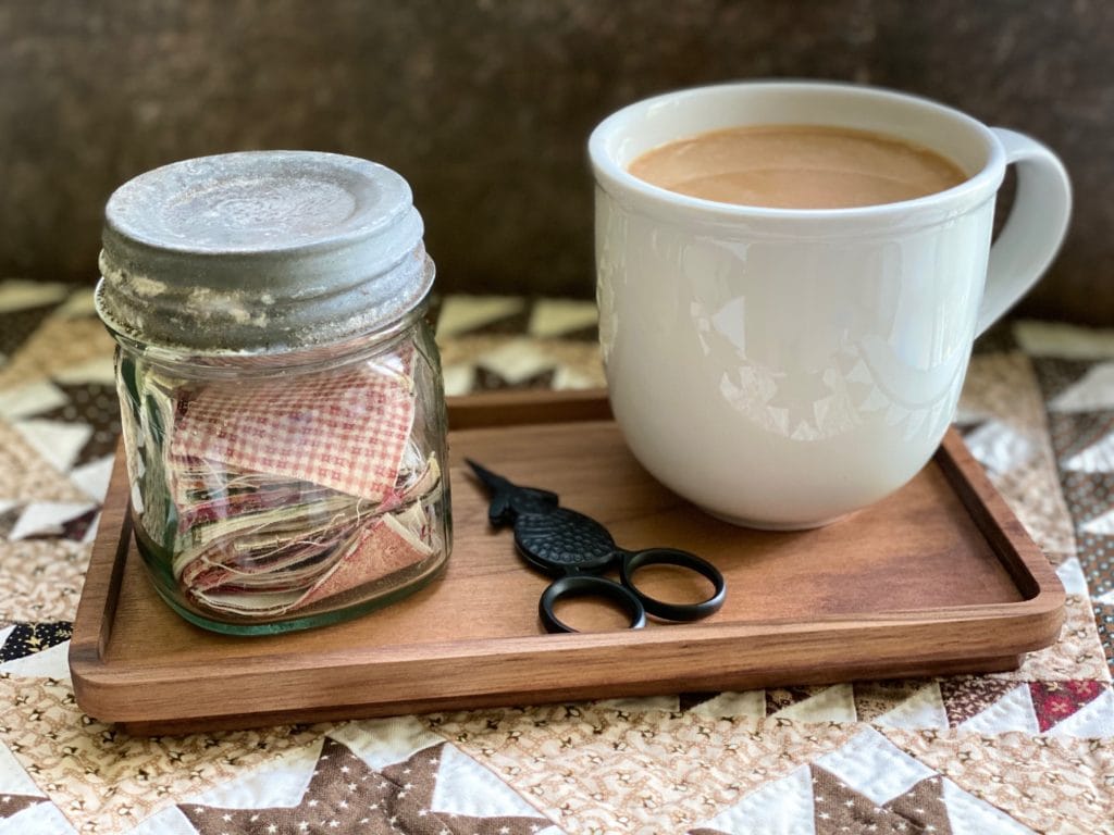 a cup of coffee and a vintage jar of squares on a wooden tray, ready for hand piecing.