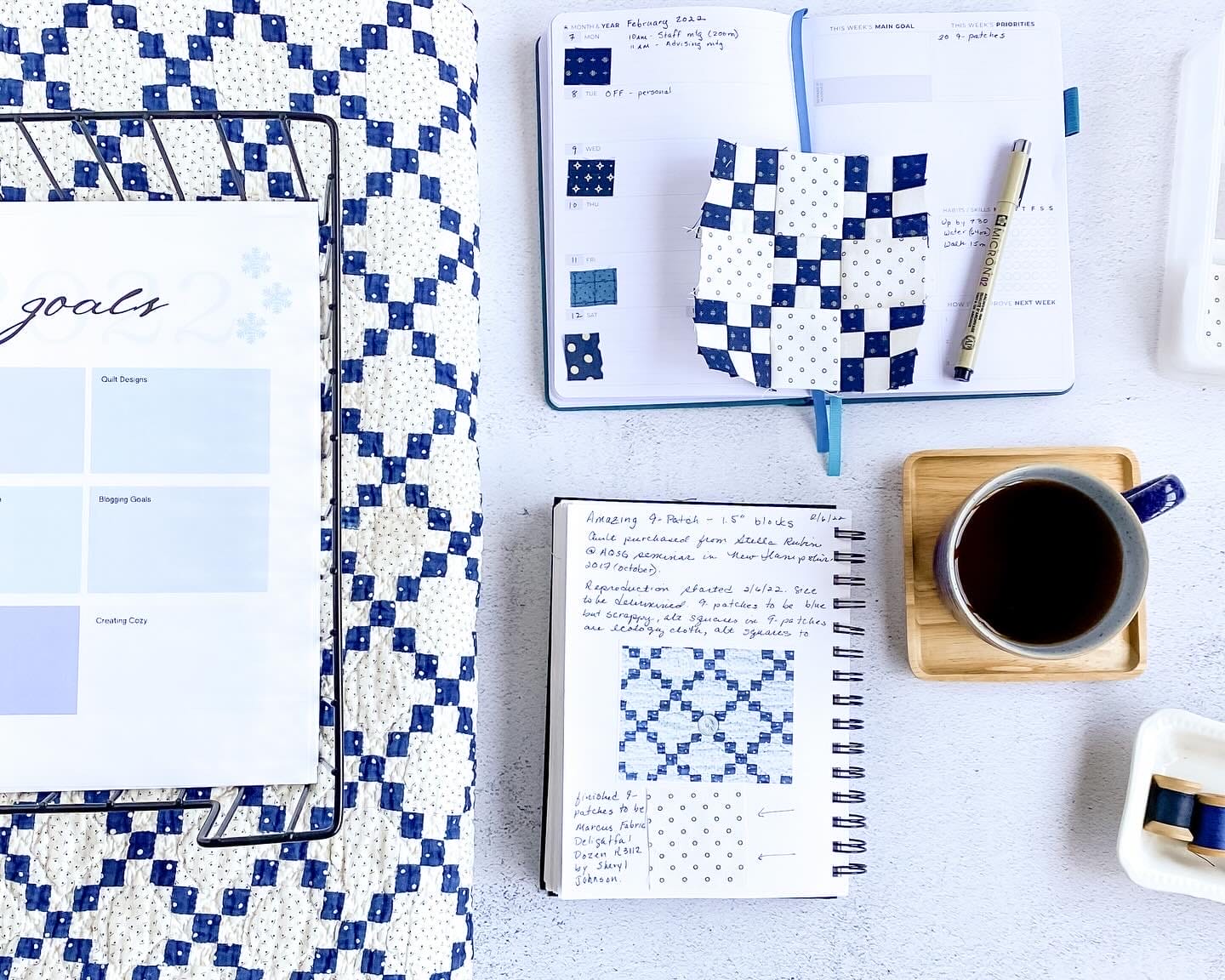 desktop with blue and white 9 patch quilt, a planner, a journal and a cup of coffee